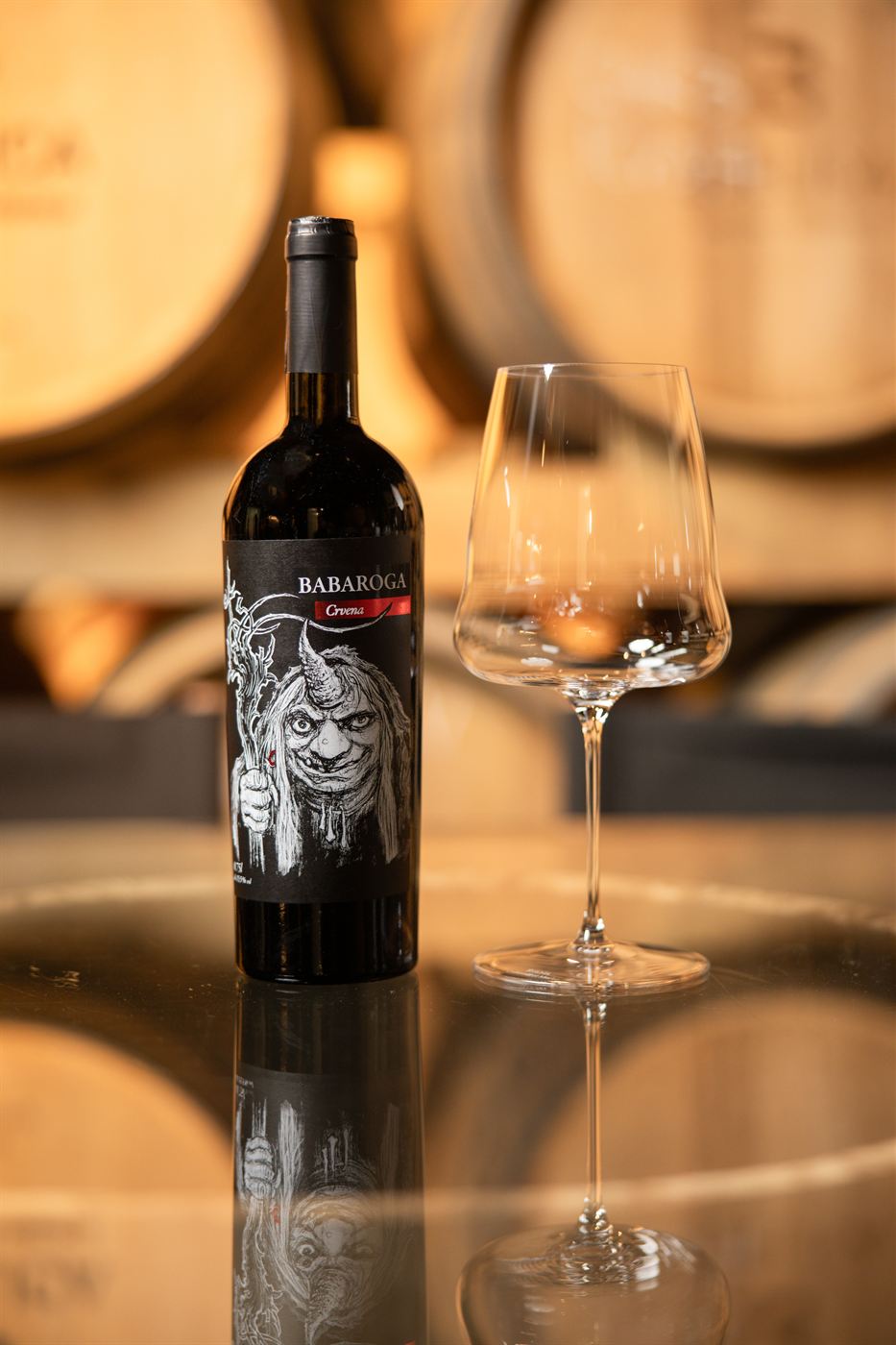 A bottle of Babaroga Crvena with a glass in front of barriques