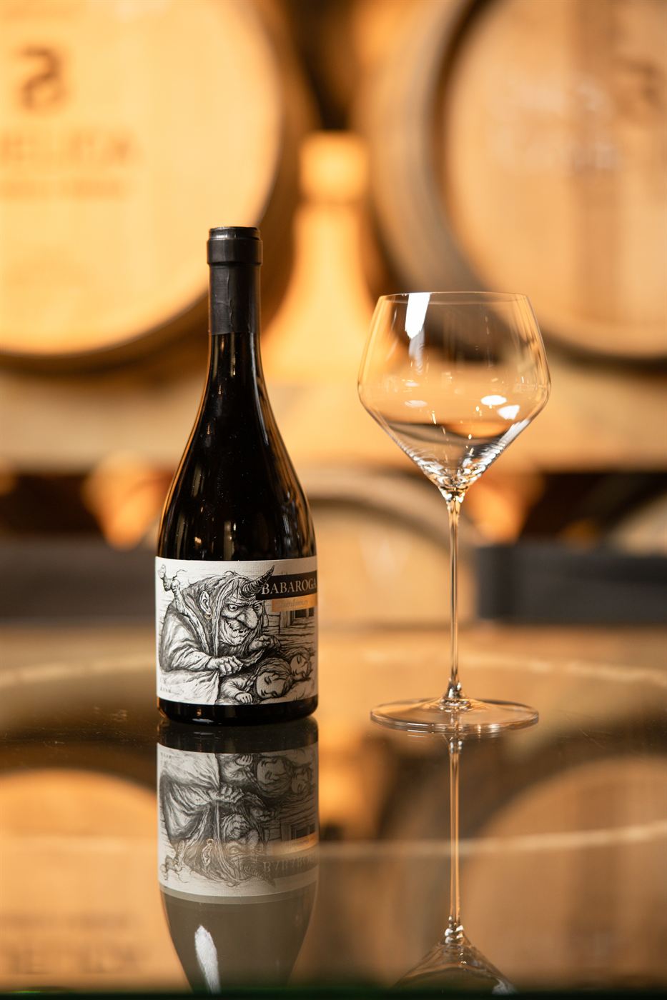 A bottle of Babaroga with a glass in front of barriques