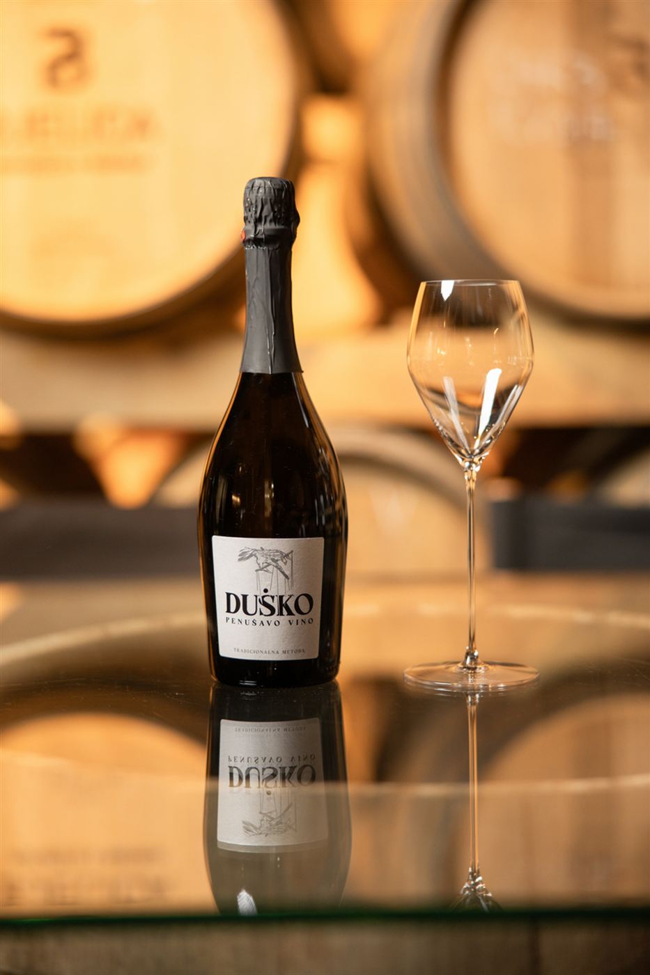Boca penušavog vina Duško sa čašom u podrumu vinarije